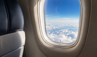 Ventana de un avión sobre las nubes con el pequeño orificio de ventilación visible en la parte inferior