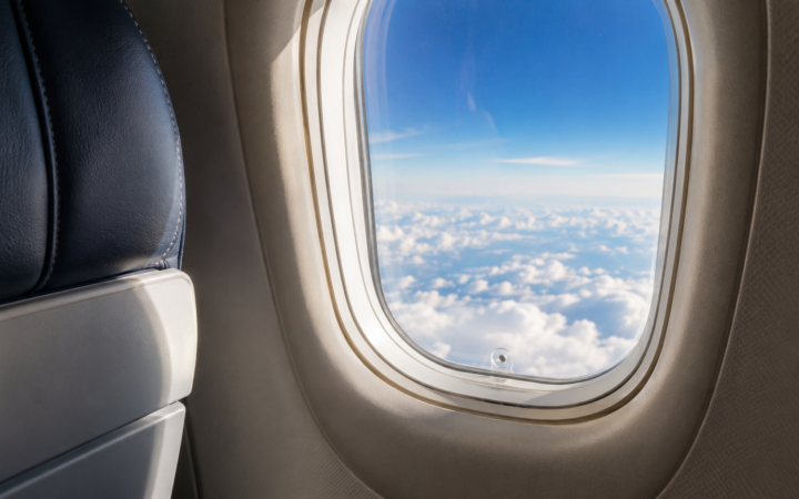 Ventana de un avión sobre las nubes con el pequeño orificio de ventilación visible en la parte inferior