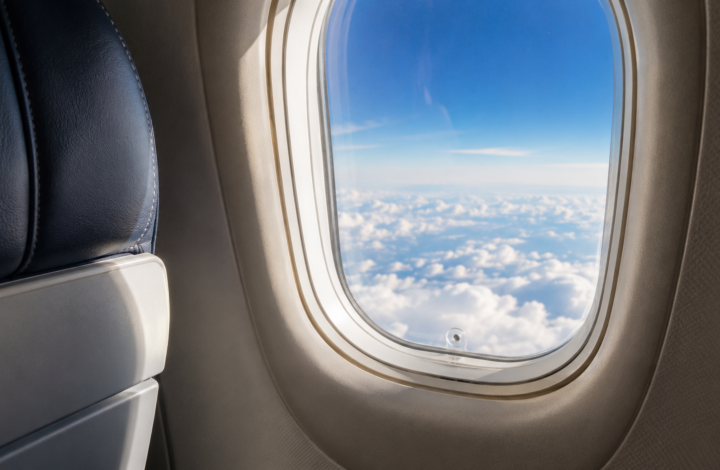 Ventana de un avión sobre las nubes con el pequeño orificio de ventilación visible en la parte inferior